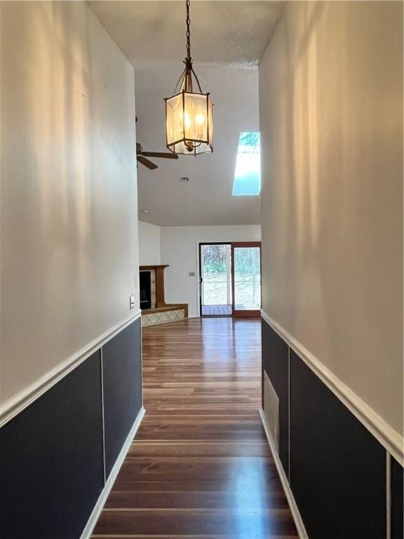 hallway featuring a wainscoted wall, dark wood-style flooring, and lofted ceiling