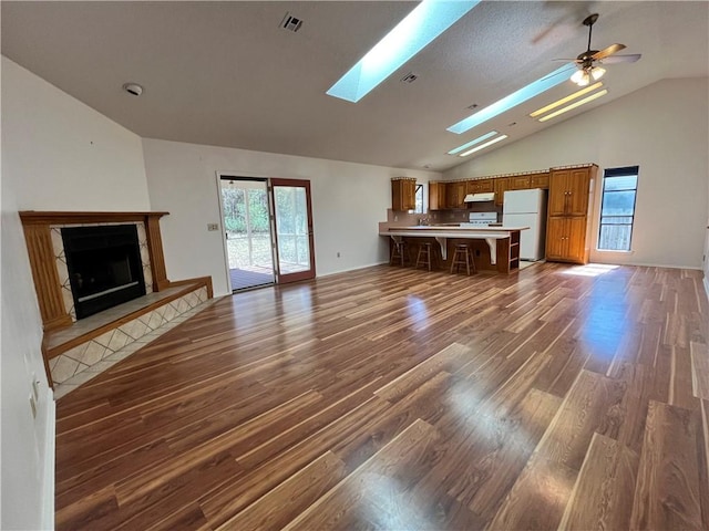 unfurnished living room featuring a fireplace with raised hearth, ceiling fan, a skylight, wood finished floors, and visible vents