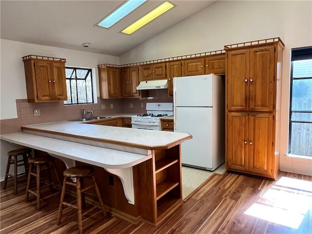 kitchen with white appliances, a peninsula, light countertops, under cabinet range hood, and a sink