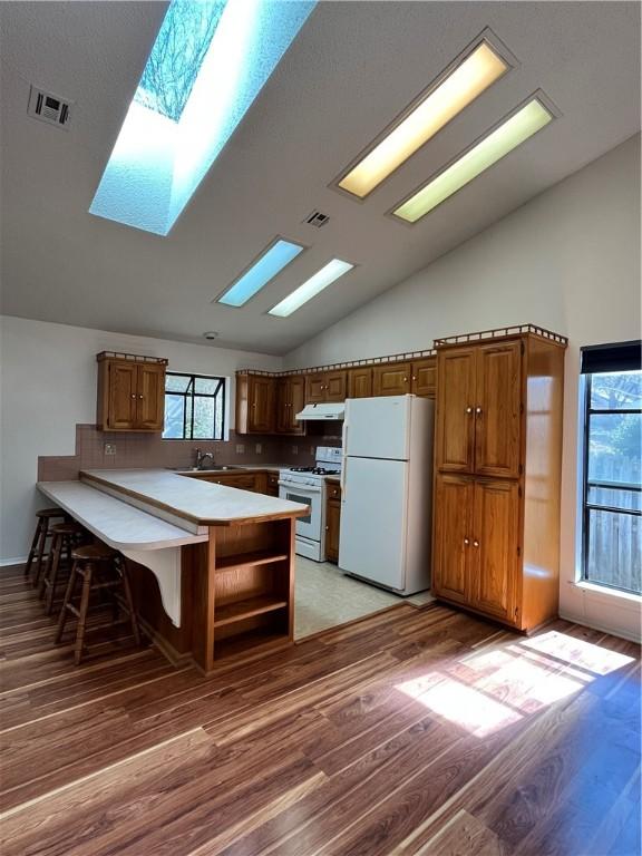 kitchen with a peninsula, white appliances, a sink, visible vents, and brown cabinets