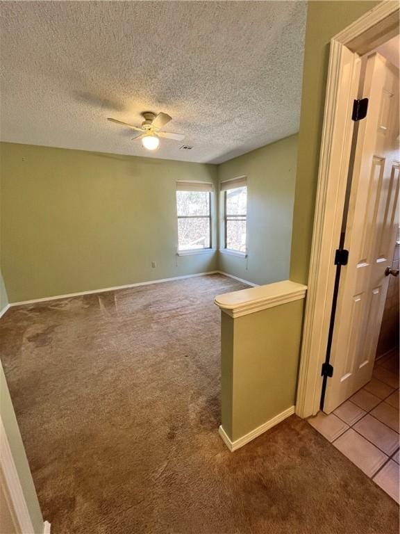 empty room featuring carpet floors, tile patterned flooring, a textured ceiling, and a ceiling fan