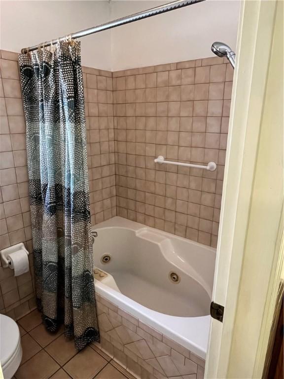 full bath featuring a combined bath / shower with jetted tub, toilet, and tile patterned floors