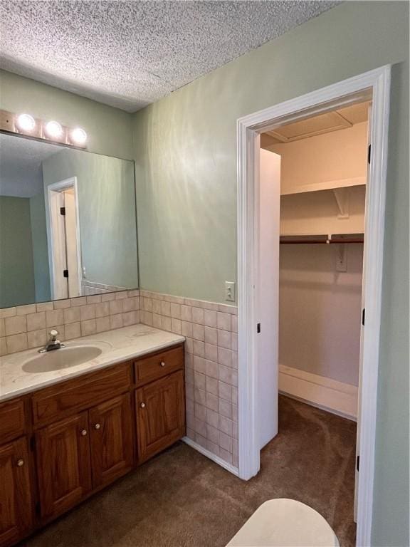 bathroom with a textured ceiling, a wainscoted wall, vanity, and tile walls