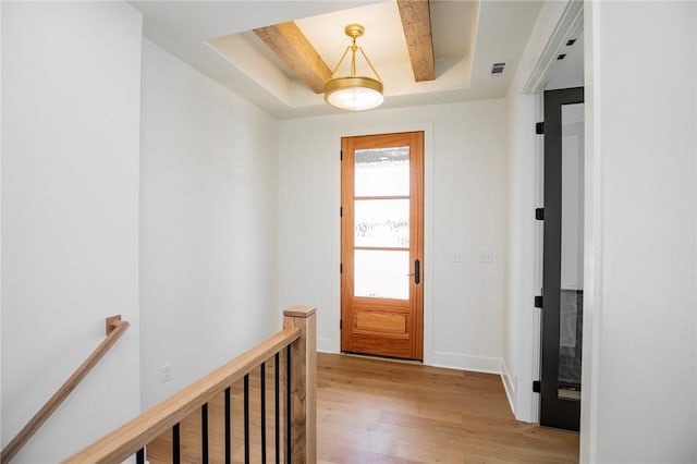 doorway to outside featuring a tray ceiling, light wood-type flooring, baseboards, and visible vents