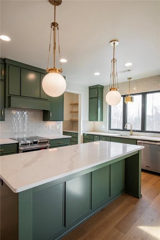 kitchen featuring a sink, light wood-style floors, appliances with stainless steel finishes, green cabinetry, and decorative backsplash