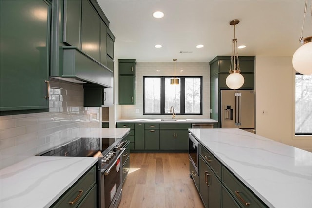 kitchen featuring light wood finished floors, green cabinetry, premium appliances, a sink, and tasteful backsplash