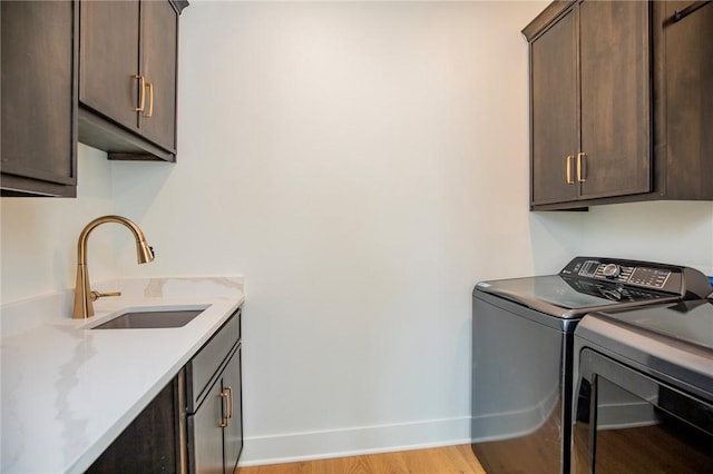 laundry room featuring baseboards, light wood-type flooring, washer and dryer, cabinet space, and a sink