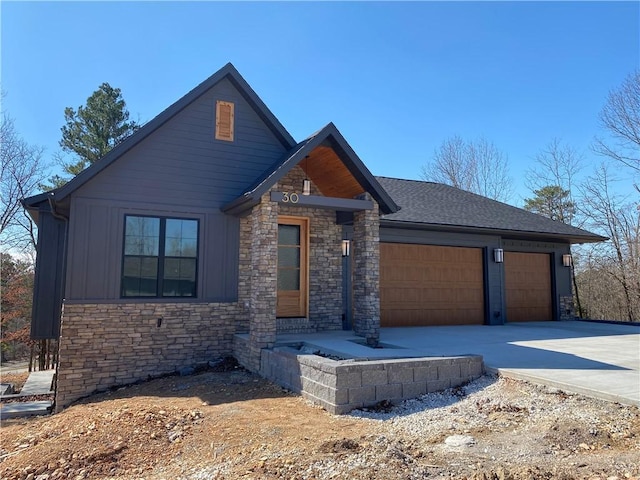 view of front of house with stone siding, an attached garage, board and batten siding, and driveway