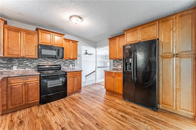 kitchen with a textured ceiling, light wood-type flooring, brown cabinets, black appliances, and tasteful backsplash