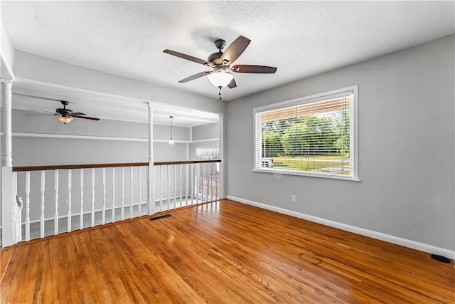 empty room with visible vents, a textured ceiling, baseboards, and wood finished floors