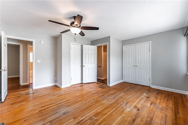 unfurnished bedroom with light wood-type flooring, a textured ceiling, baseboards, and two closets