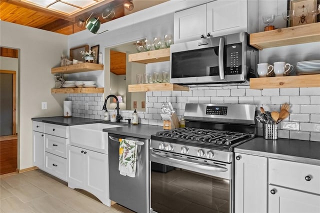 kitchen featuring open shelves, a sink, dark countertops, backsplash, and stainless steel appliances