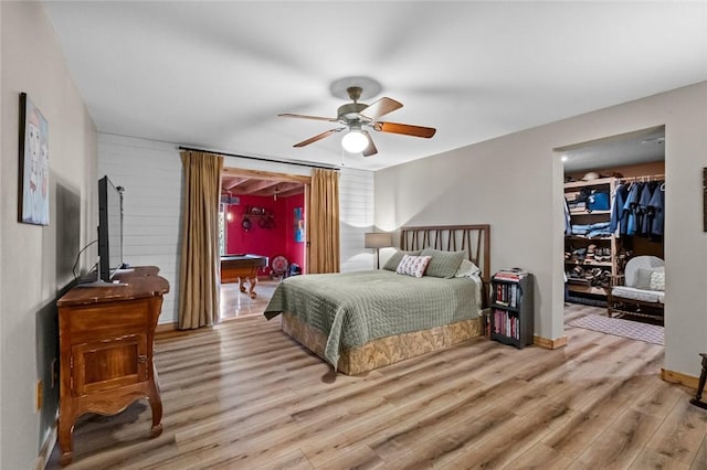 bedroom with light wood-style flooring, a spacious closet, and a ceiling fan