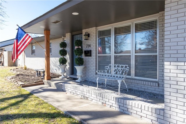 entrance to property featuring visible vents, brick siding, and a porch