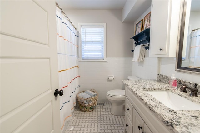 bathroom with vanity, a shower with shower curtain, wainscoting, tile walls, and toilet