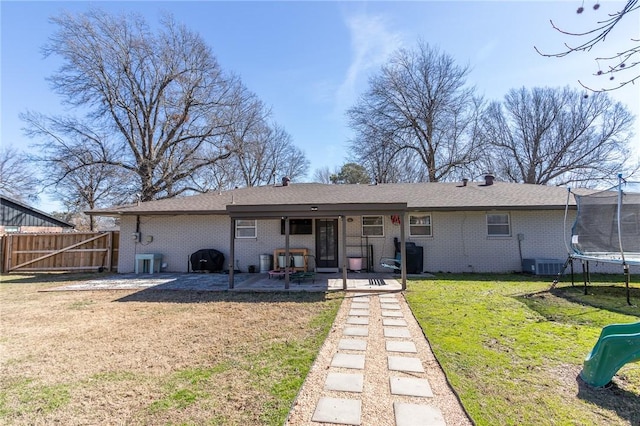 rear view of house with a lawn, a trampoline, fence, brick siding, and a patio area