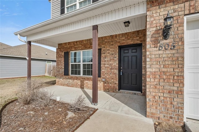 view of exterior entry with a garage, covered porch, and brick siding