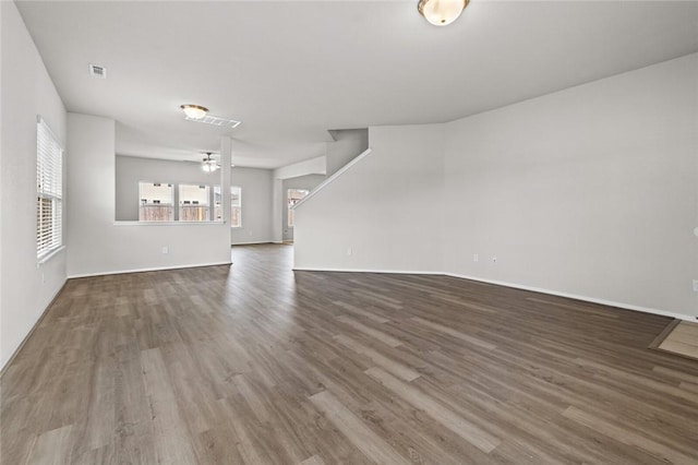 unfurnished living room featuring wood finished floors, visible vents, baseboards, stairs, and a ceiling fan