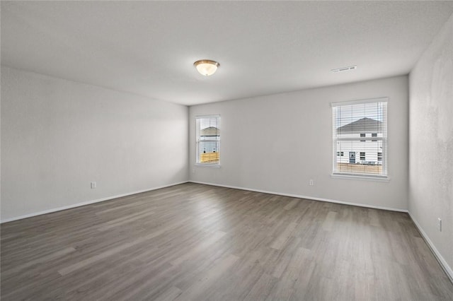 unfurnished room featuring dark wood-style flooring, baseboards, and visible vents