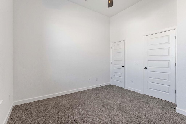 unfurnished room featuring ceiling fan, dark carpet, and baseboards