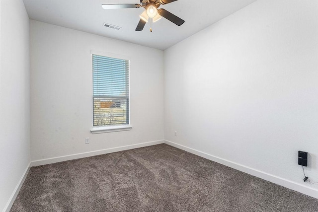 empty room with a ceiling fan, dark carpet, visible vents, and baseboards