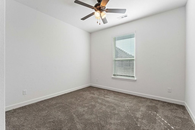 spare room with dark colored carpet, visible vents, ceiling fan, and baseboards