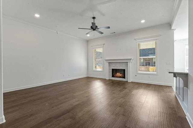 unfurnished living room featuring a warm lit fireplace, ceiling fan, dark wood-style flooring, baseboards, and ornamental molding