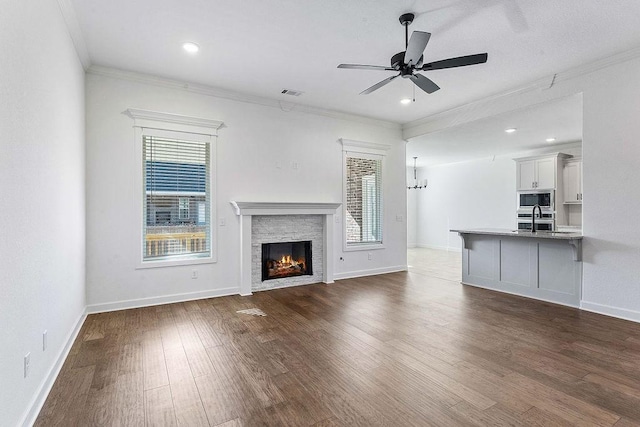 unfurnished living room featuring dark wood finished floors, crown molding, visible vents, a warm lit fireplace, and ceiling fan with notable chandelier