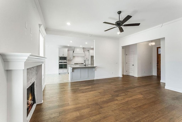 unfurnished living room featuring a warm lit fireplace, ornamental molding, a sink, and wood finished floors