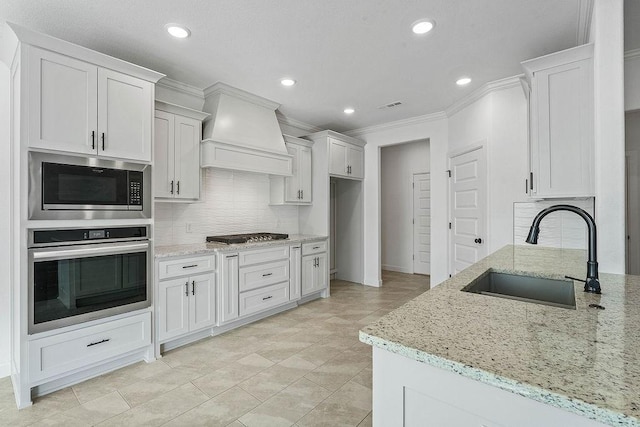 kitchen featuring light stone counters, visible vents, appliances with stainless steel finishes, a sink, and premium range hood