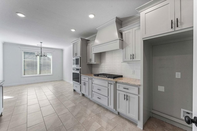 kitchen featuring decorative backsplash, custom range hood, appliances with stainless steel finishes, hanging light fixtures, and light stone countertops