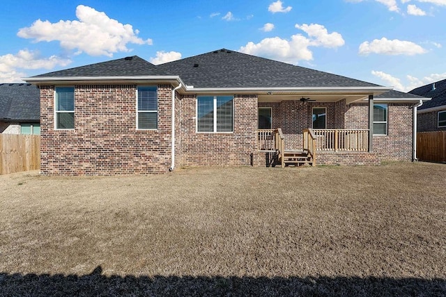 rear view of house featuring brick siding, roof with shingles, and fence