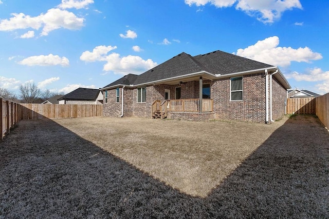 rear view of house featuring a shingled roof, brick siding, and a fenced backyard