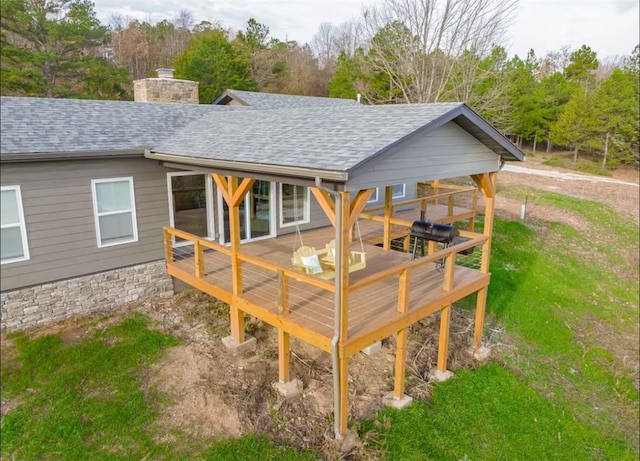 rear view of property featuring a wooden deck, a chimney, and roof with shingles