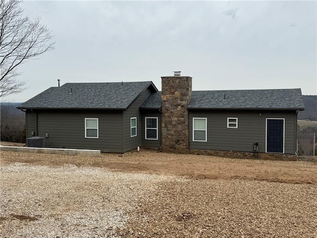 back of property with a shingled roof, cooling unit, and a chimney