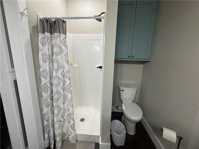 bathroom with a stall shower, toilet, and baseboards