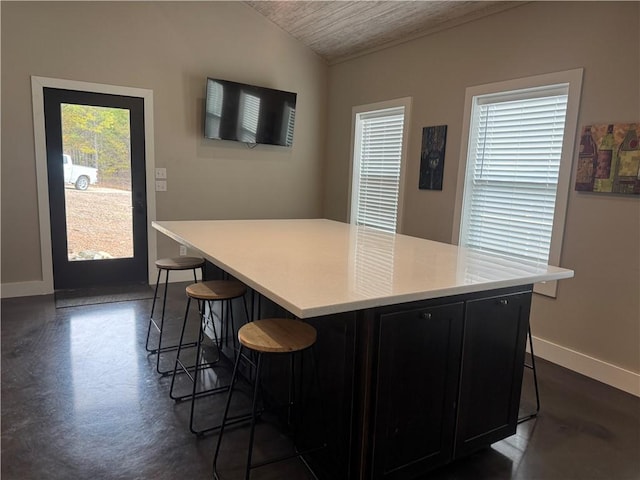 kitchen featuring a center island, light countertops, vaulted ceiling, dark cabinets, and a kitchen bar