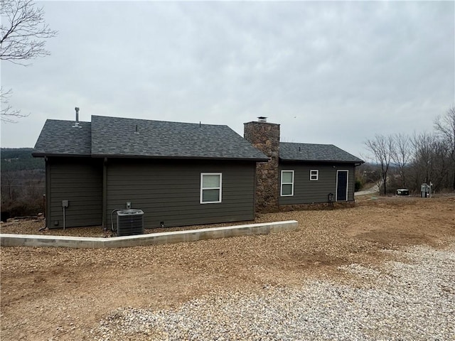 back of property with a shingled roof, a chimney, and cooling unit