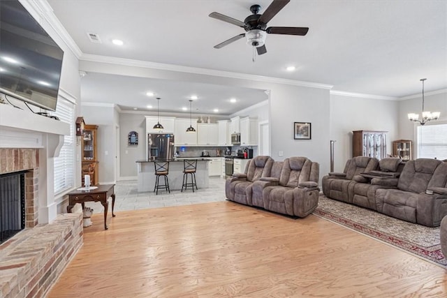 living area featuring light wood-style flooring, ceiling fan with notable chandelier, crown molding, a fireplace, and recessed lighting