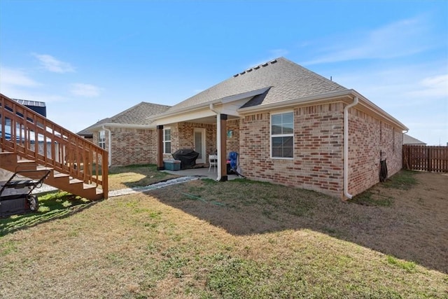 rear view of property with brick siding, a lawn, stairway, a patio area, and fence