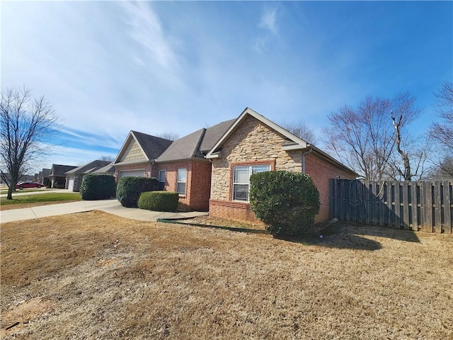 view of front of home with brick siding, fence, a garage, stone siding, and driveway