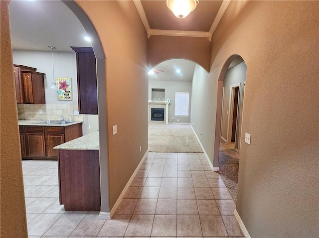 hallway featuring arched walkways, crown molding, baseboards, and light tile patterned floors