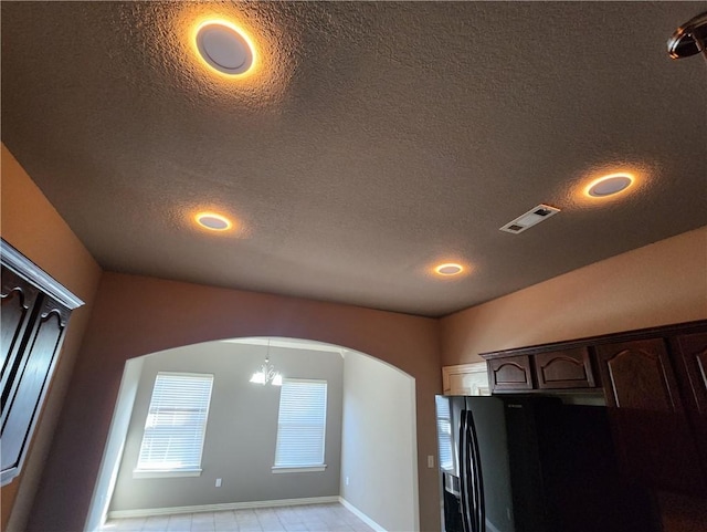 details featuring arched walkways, visible vents, black fridge with ice dispenser, a textured ceiling, and dark brown cabinets