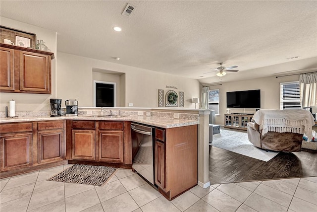 kitchen with a peninsula, a sink, open floor plan, stainless steel dishwasher, and brown cabinets