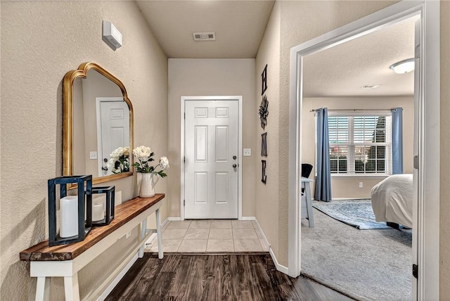 interior space featuring visible vents, a textured wall, baseboards, and wood finished floors