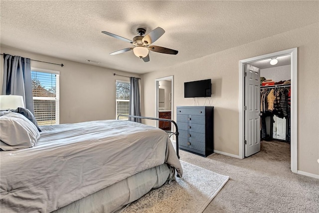 bedroom featuring baseboards, a walk in closet, a textured ceiling, and light colored carpet