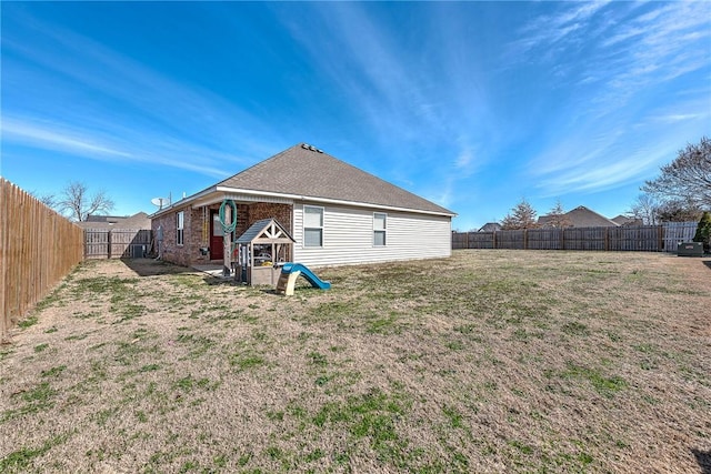 rear view of house featuring a yard, brick siding, and a fenced backyard