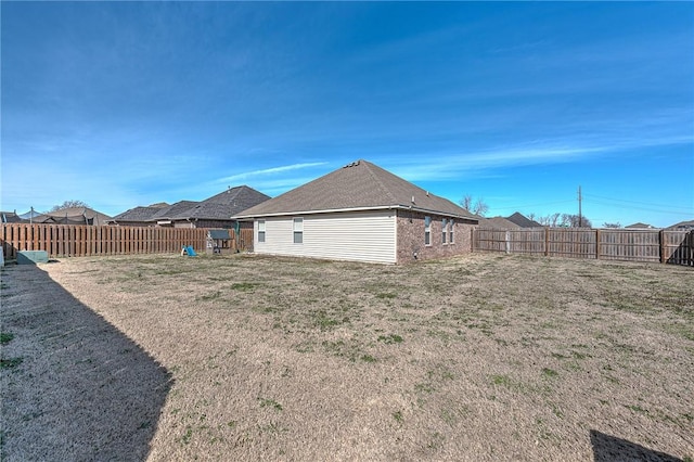 rear view of property featuring brick siding, a lawn, and a fenced backyard