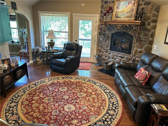 living room featuring arched walkways, a fireplace, wood finished floors, baseboards, and vaulted ceiling