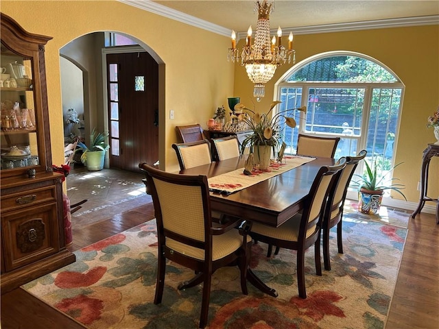 dining space featuring an inviting chandelier, arched walkways, wood finished floors, and ornamental molding